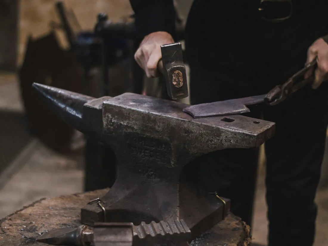 Martillo sobre un yunque con una pletina de acero sujeta con tenazas en un taller de forja